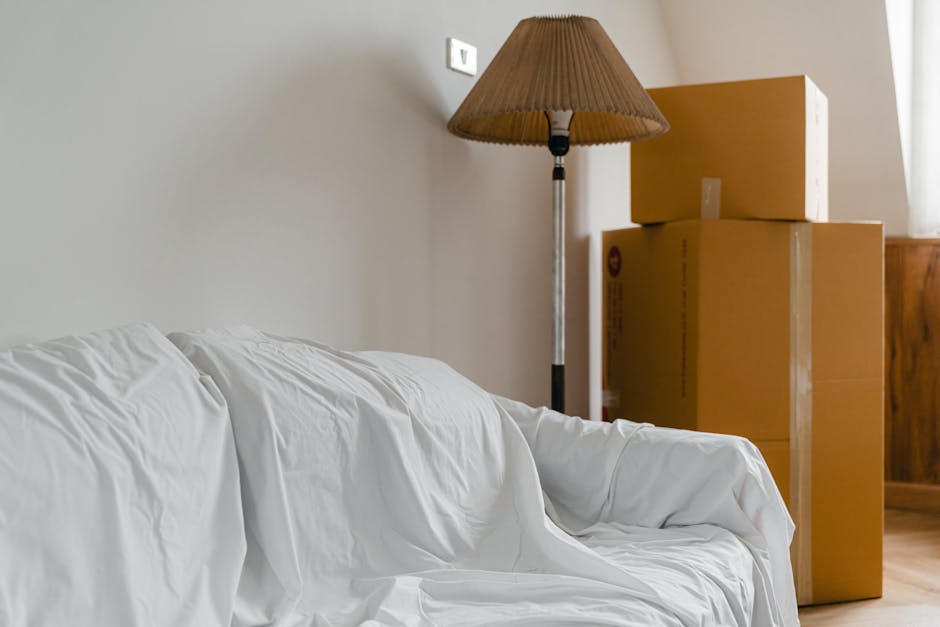 A person using a handheld vacuum cleaner to deep clean a decorative yellow and white patterned cushion placed on a dark fabric sofa in a residential living room. The scene captures the process of surf